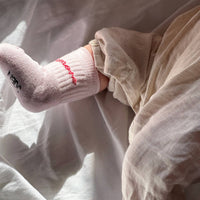 Close-up of a child's legs wearing pink socks with red accents on a white blanket.